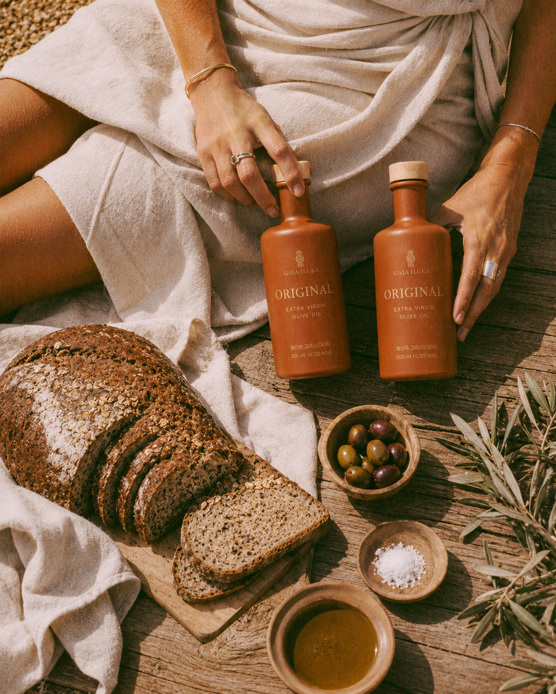 Gaia Iluka Original bottles on a wooden board with bread, olives and olive branches